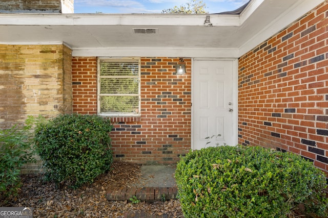 doorway to property featuring brick siding and visible vents