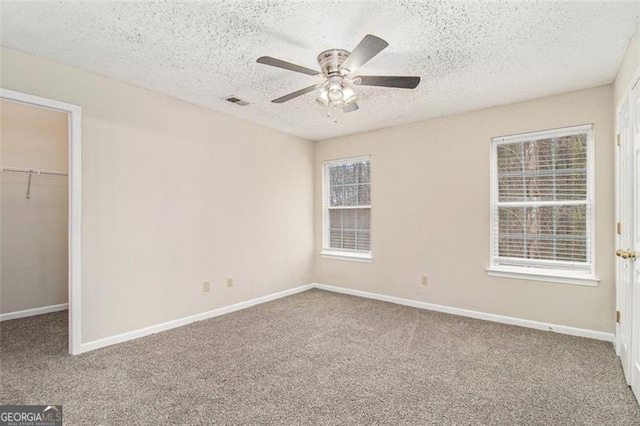 unfurnished bedroom featuring baseboards, carpet, a walk in closet, a textured ceiling, and a closet