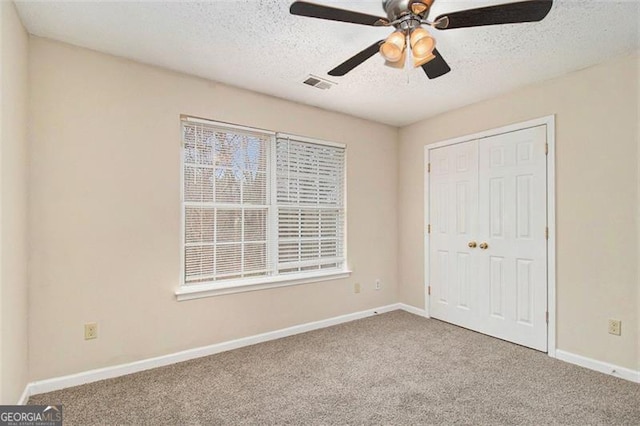 unfurnished bedroom with a textured ceiling, carpet flooring, visible vents, baseboards, and a closet