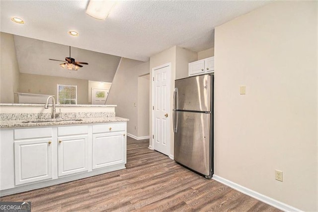 kitchen with baseboards, wood finished floors, freestanding refrigerator, white cabinetry, and a sink