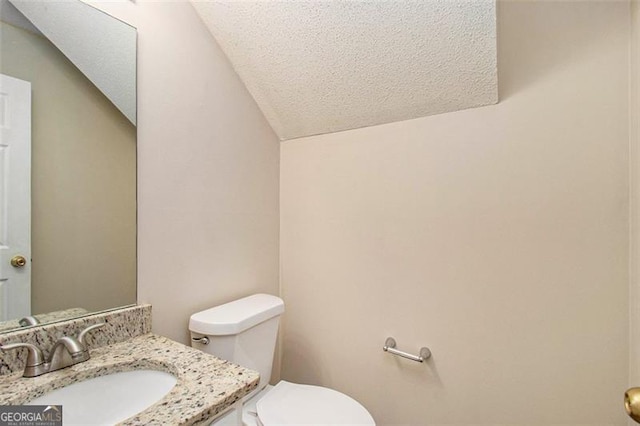 bathroom featuring toilet, vaulted ceiling, a textured ceiling, and vanity