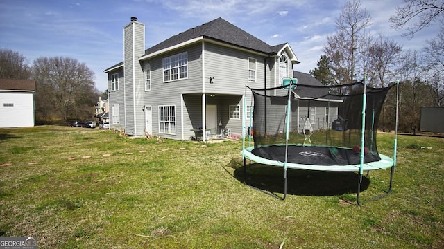 rear view of property featuring a trampoline, a chimney, and a lawn