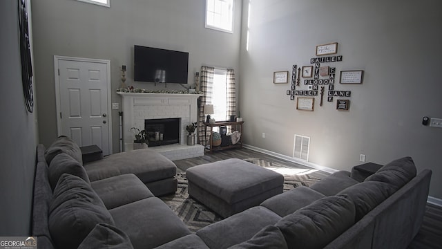 living room with a brick fireplace, visible vents, dark wood finished floors, and a towering ceiling