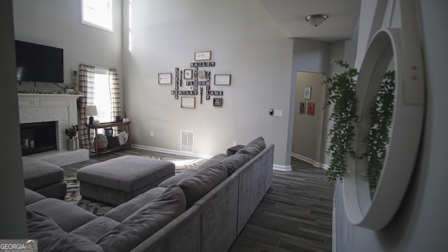 living room featuring a brick fireplace, dark wood-style floors, visible vents, and a wealth of natural light