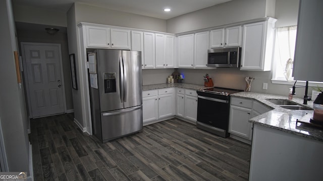 kitchen featuring stainless steel appliances, a sink, white cabinetry, light stone countertops, and dark wood finished floors