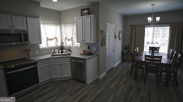 kitchen with dark wood-style flooring, stainless steel appliances, hanging light fixtures, a sink, and baseboards