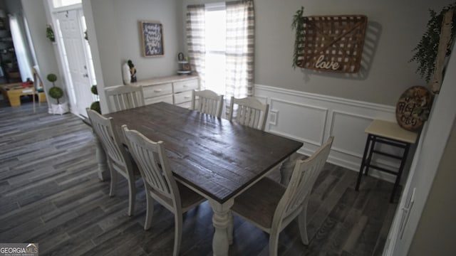 dining space featuring a wainscoted wall, dark wood-style flooring, and a decorative wall