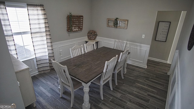 dining area featuring dark wood-style floors, a decorative wall, and a wainscoted wall