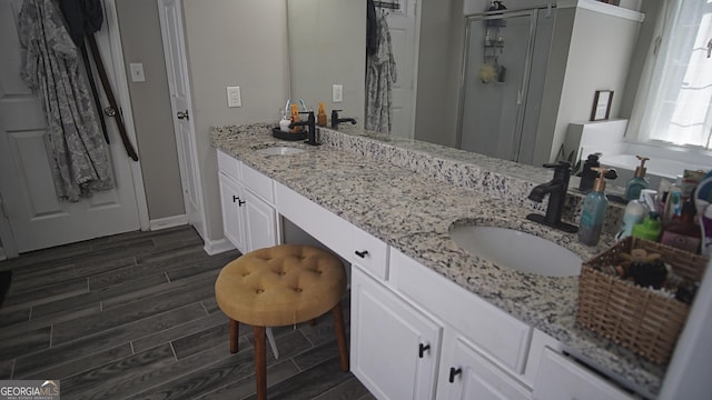 full bathroom with double vanity, a stall shower, wood tiled floor, and a sink