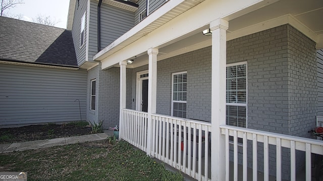 view of side of home with brick siding, covered porch, and roof with shingles