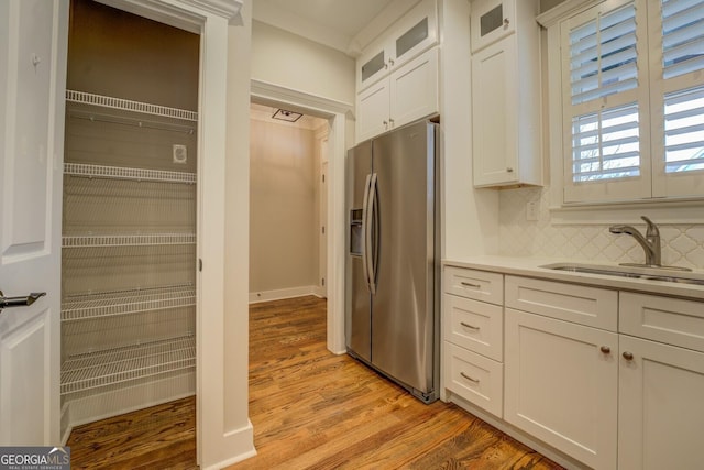 kitchen featuring light wood finished floors, glass insert cabinets, white cabinetry, a sink, and stainless steel fridge