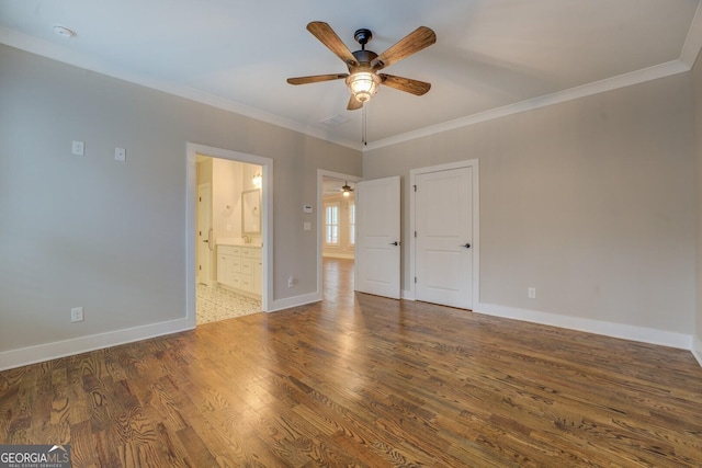 unfurnished bedroom featuring crown molding, ensuite bathroom, a ceiling fan, wood finished floors, and baseboards