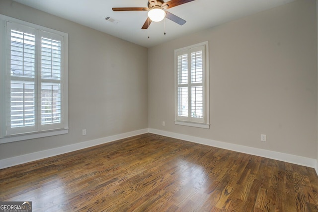 empty room with a wealth of natural light, visible vents, baseboards, and wood finished floors