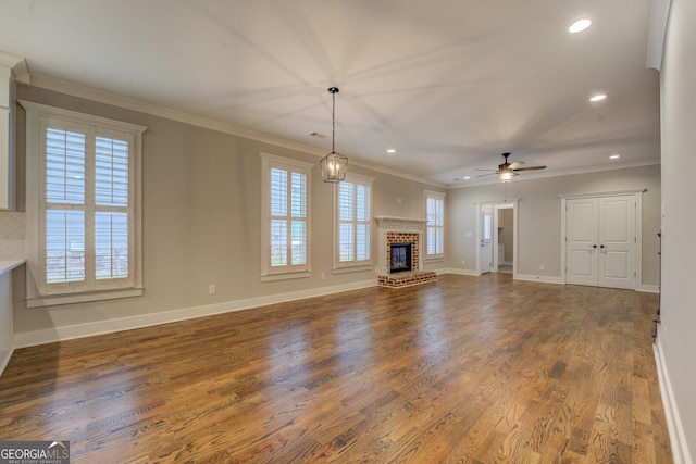 unfurnished living room with dark wood finished floors, a brick fireplace, crown molding, and recessed lighting