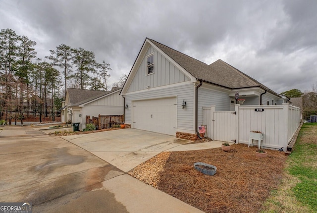 view of side of home featuring board and batten siding, concrete driveway, a shingled roof, and fence