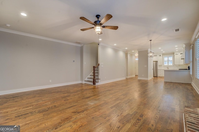 unfurnished living room featuring visible vents, ornamental molding, ceiling fan, wood finished floors, and baseboards