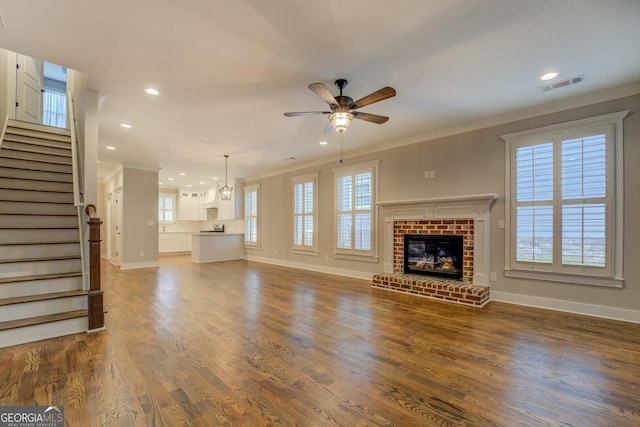 unfurnished living room with dark wood finished floors, visible vents, ornamental molding, a brick fireplace, and stairs