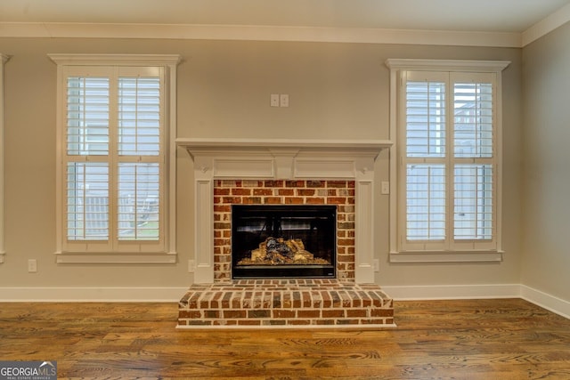 interior details with ornamental molding, a brick fireplace, baseboards, and wood finished floors