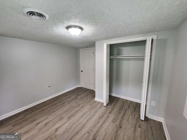 unfurnished bedroom featuring a closet, visible vents, baseboards, and wood finished floors