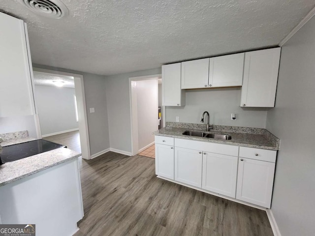 kitchen featuring a textured ceiling, a sink, visible vents, white cabinets, and light wood-style floors