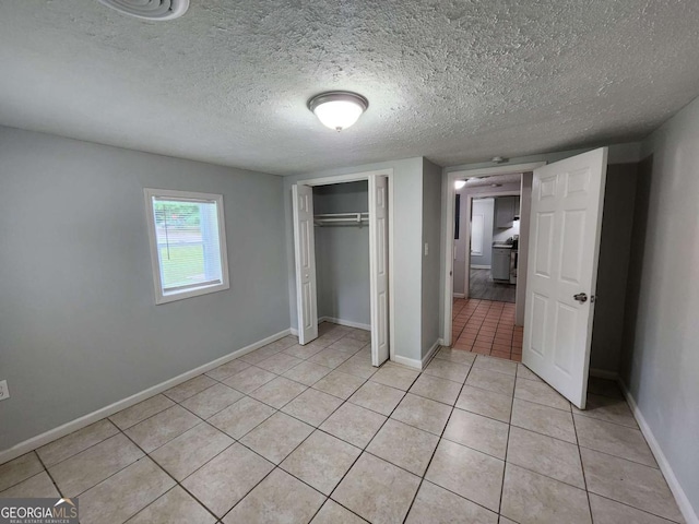 unfurnished bedroom featuring a closet, a textured ceiling, baseboards, and light tile patterned floors