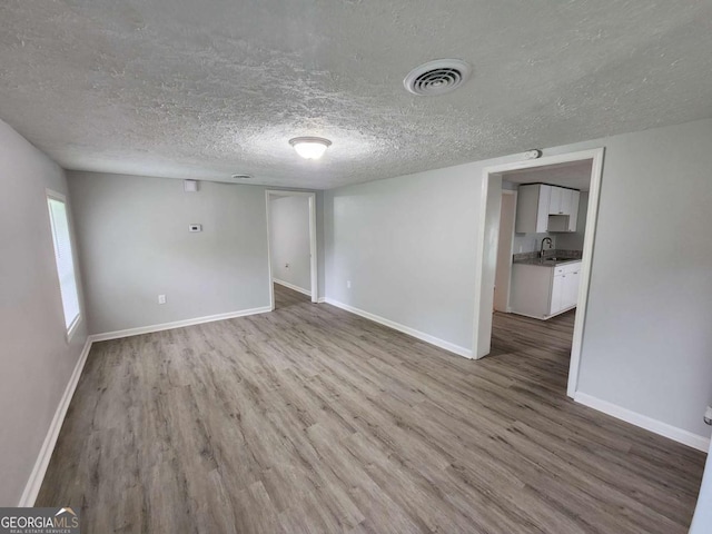 empty room with a textured ceiling, wood finished floors, a sink, visible vents, and baseboards