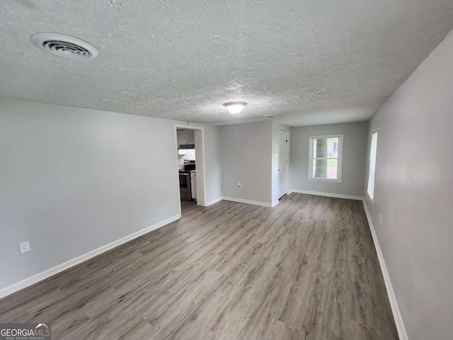 unfurnished room with visible vents, a textured ceiling, baseboards, and wood finished floors