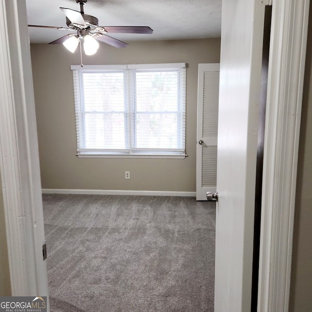 carpeted spare room featuring baseboards and a ceiling fan