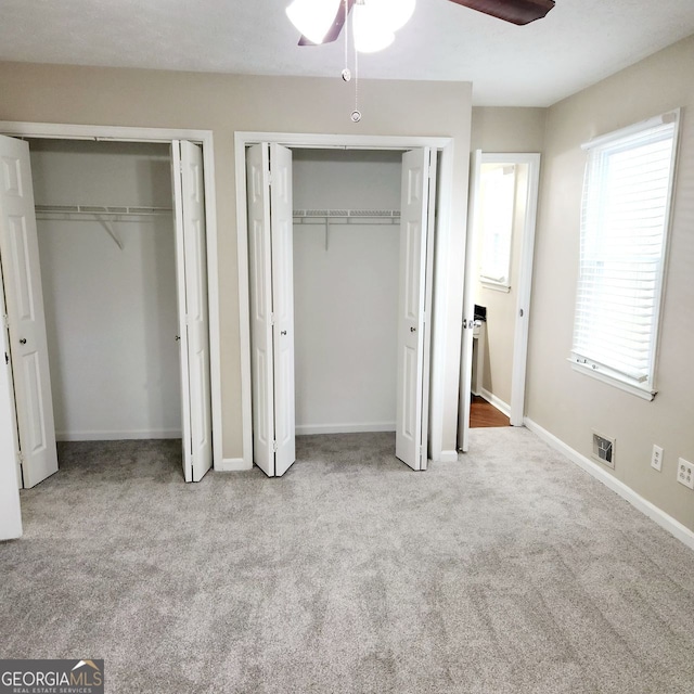 unfurnished bedroom with visible vents, two closets, a ceiling fan, carpet flooring, and baseboards