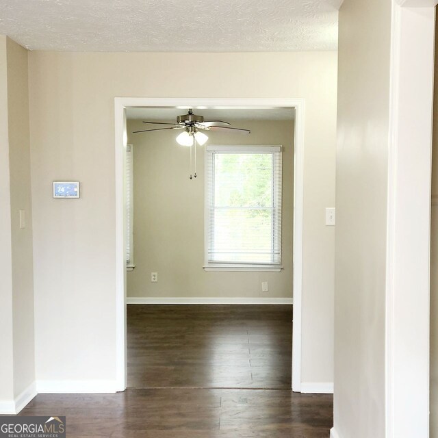 spare room with ceiling fan, a textured ceiling, dark wood-type flooring, and baseboards