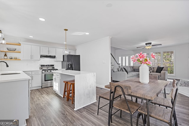 kitchen with a center island, light countertops, black refrigerator with ice dispenser, stainless steel range oven, and a sink