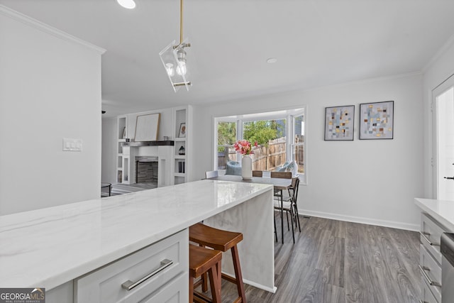 kitchen with baseboards, dark wood finished floors, crown molding, a fireplace, and pendant lighting