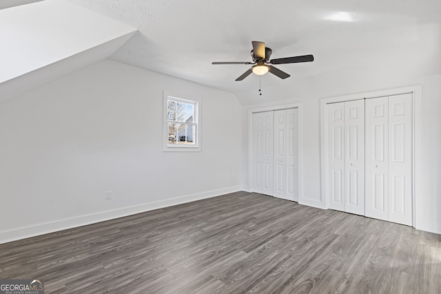 unfurnished bedroom featuring lofted ceiling, dark wood-style floors, baseboards, and multiple closets