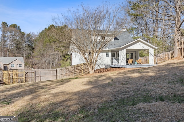 rear view of property with a deck, roof with shingles, a lawn, and fence