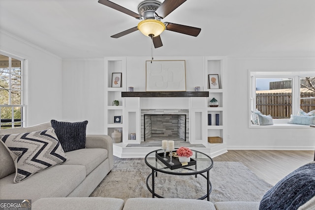 living area featuring crown molding, a fireplace with raised hearth, a wealth of natural light, and wood finished floors