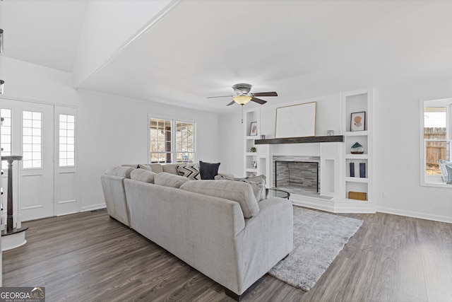 living area featuring dark wood-style floors, a fireplace with raised hearth, plenty of natural light, and ceiling fan