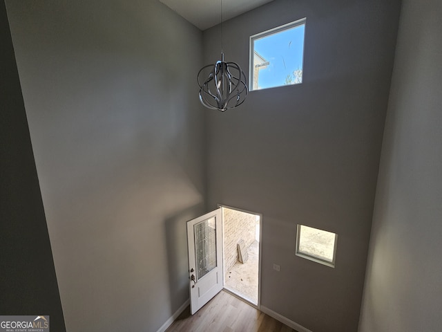 foyer featuring a chandelier, wood finished floors, a towering ceiling, and baseboards