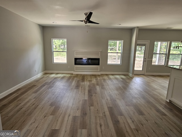 unfurnished living room with a glass covered fireplace, a healthy amount of sunlight, and wood finished floors