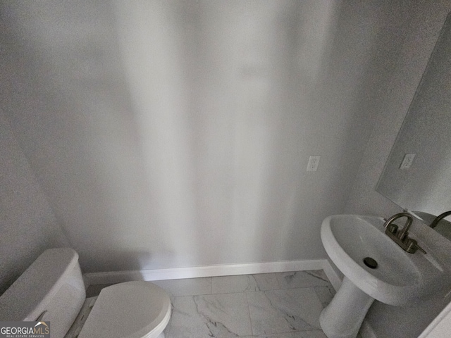 half bathroom featuring toilet, marble finish floor, baseboards, and a sink