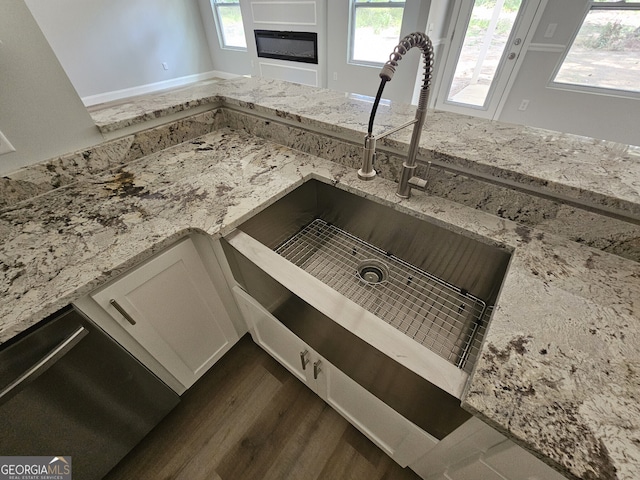 interior details with a glass covered fireplace, dark wood-type flooring, light stone countertops, white cabinetry, and a sink