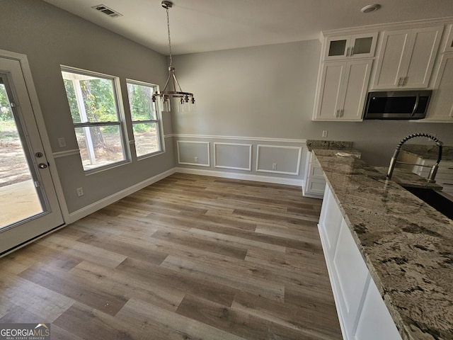 unfurnished dining area with wainscoting, an inviting chandelier, visible vents, and light wood-style floors