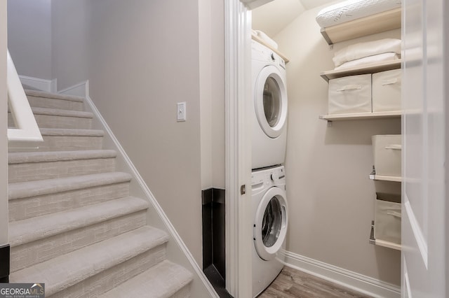 washroom with baseboards, wood finished floors, laundry area, and stacked washer / dryer