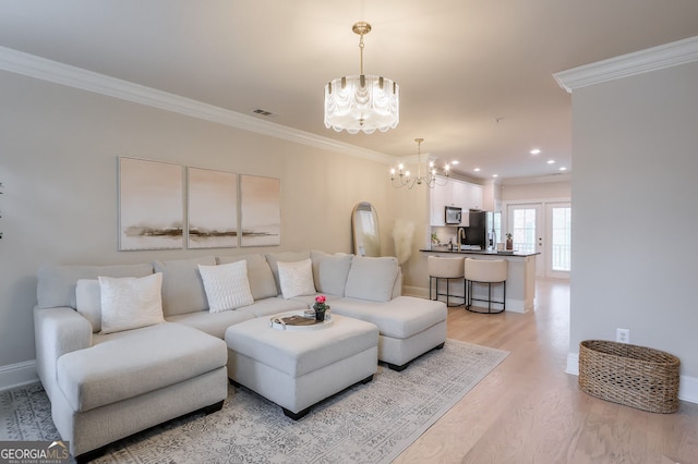 living room with a notable chandelier, light wood-style flooring, crown molding, and visible vents