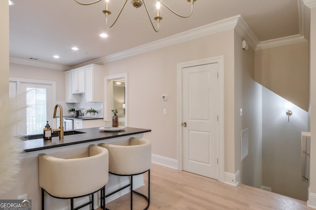 kitchen with dark countertops, a breakfast bar, ornamental molding, and white cabinetry