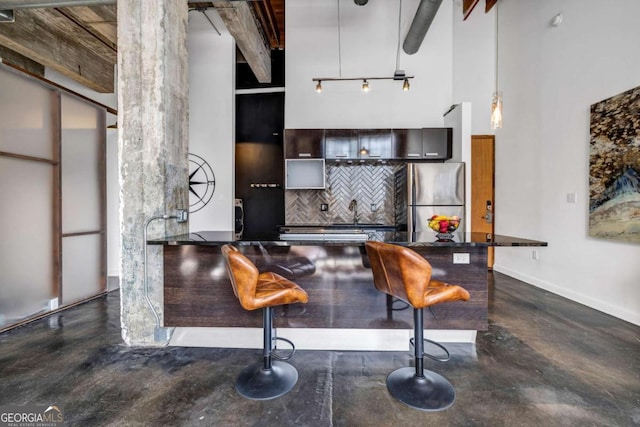 kitchen with concrete flooring, freestanding refrigerator, backsplash, and a towering ceiling