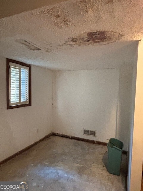 empty room featuring unfinished concrete flooring, baseboards, visible vents, and a textured ceiling