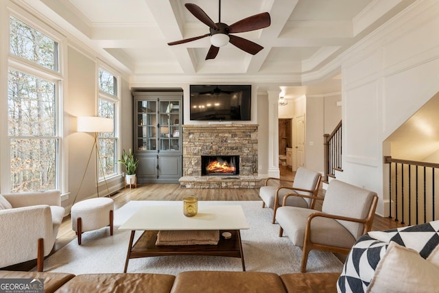 interior space with crown molding, beamed ceiling, a stone fireplace, wood finished floors, and coffered ceiling