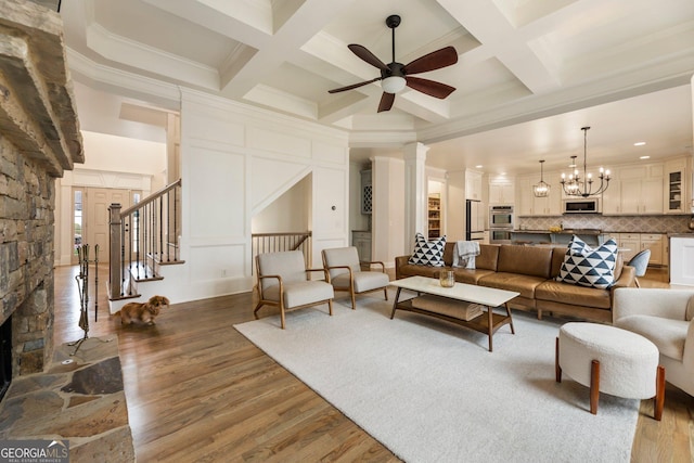 living area featuring beamed ceiling, ceiling fan with notable chandelier, stairway, and wood finished floors