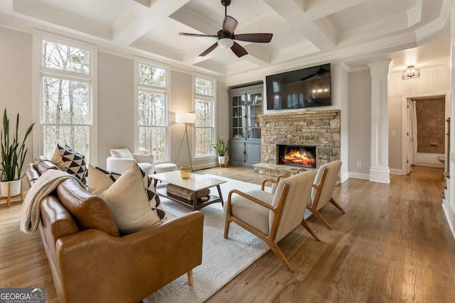 living room featuring beamed ceiling, ornate columns, a stone fireplace, wood finished floors, and a ceiling fan