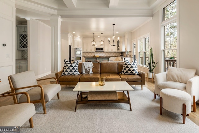 living room with beam ceiling, light wood-style flooring, ornamental molding, decorative columns, and a chandelier